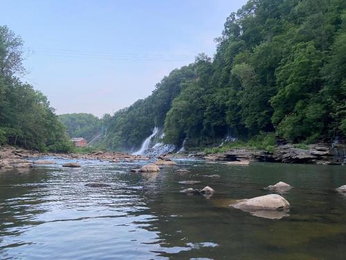 A serene river scene with a waterfall cascading down rocky cliffs, surrounded by lush green trees.