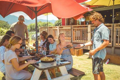 A group of friends enjoying a meal outdoors at a restaurant, with colorful umbrellas and a scenic backdrop.