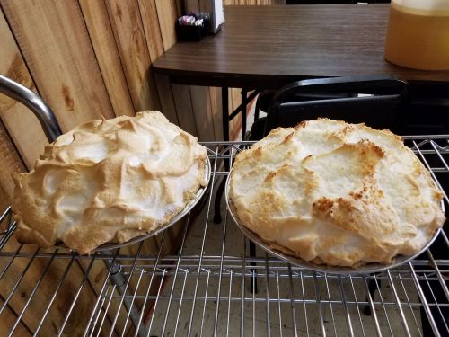 Two freshly baked meringue pies on a wire rack, one lightly browned and the other with a golden, toasted top.