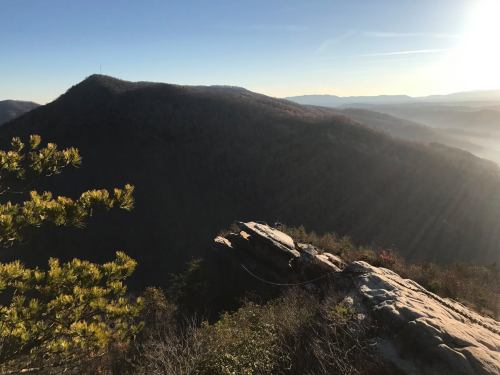 A scenic view of mountains at sunrise, with rocky outcrops and trees in the foreground.