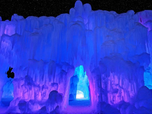 A stunning ice cave illuminated with blue and purple lights, creating a magical, otherworldly atmosphere.