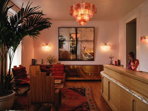 A stylish lobby with warm lighting, modern furniture, and a reception desk, featuring a large mirror and decorative plants.