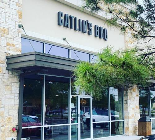 Exterior of Gatlin's BBQ restaurant with a stone facade and large windows, featuring a sign above the entrance.