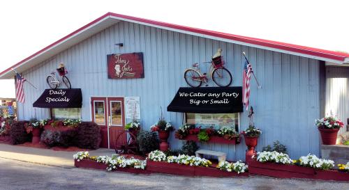 A charming restaurant exterior with flower beds, awnings, and bicycles, featuring signs for daily specials and catering.
