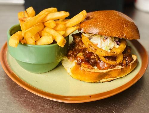 A BBQ chicken sandwich with onion rings and coleslaw, served with a side of golden French fries.