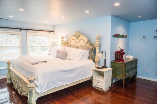 Cozy bedroom with a large bed, blue walls, hardwood floors, and decorative accents, including a vintage nightstand.