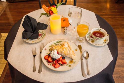 A beautifully set table with a croissant, berries, whipped cream, juice, tea, and decorative elements.