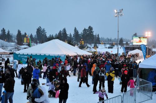 A large crowd gathers at a snowy outdoor event, with tents and trees in the background under a gray sky.