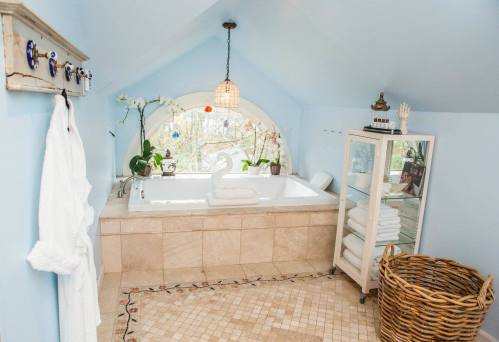 Bright bathroom with a large tub, blue walls, plants, and a wicker basket, featuring a cozy, inviting atmosphere.