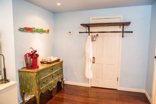 A cozy room with blue walls, a wooden dresser, a robe hanging on a rack, and a door leading to another space.