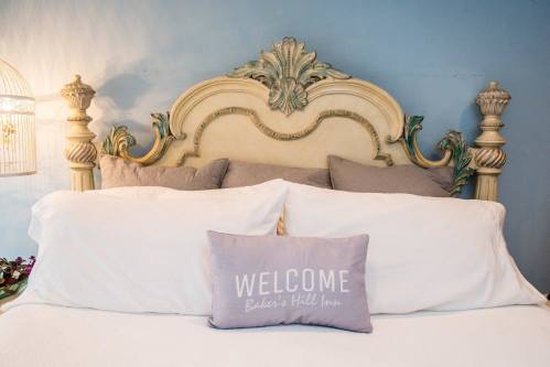 A beautifully styled bed with decorative pillows and a "WELCOME" cushion against a blue wall.