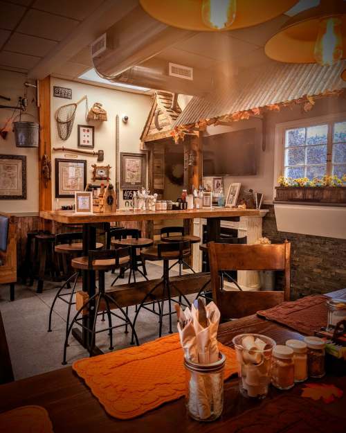 Cozy restaurant interior with wooden tables, stools, and warm lighting, featuring rustic decor and autumn accents.