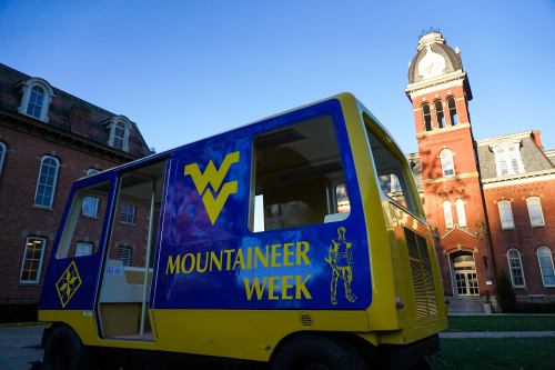 A colorful vehicle promoting "Mountaineer Week" in front of a historic building with a clock tower.