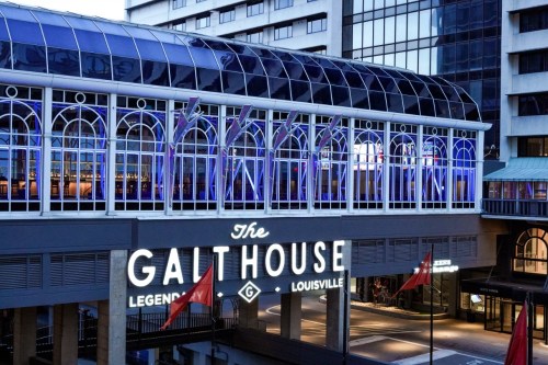 The Galt House hotel in Louisville, illuminated at night with blue lights and a modern glass structure.