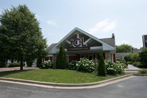 Exterior view of The Champagne Lodge, featuring a sign and landscaped entrance on a sunny day.