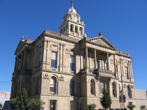 Historic stone courthouse with a clock tower, featuring ornate architectural details against a clear blue sky.
