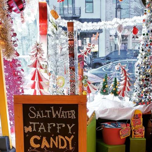 Colorful candy shop window decorated for the holidays, featuring a sign for saltwater taffy and festive decorations.