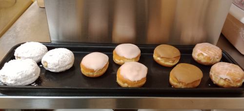 A tray of assorted donuts: two powdered sugar, four with pink, brown, and white icing, all filled with cream.