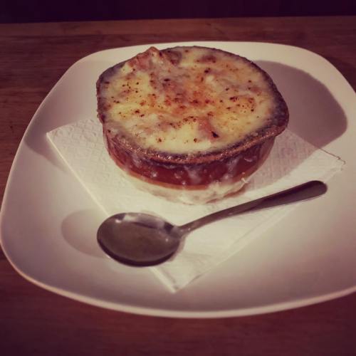 A bowl of creamy baked dish topped with melted cheese, served on a white plate with a spoon beside it.