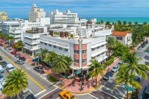 Aerial view of a vibrant Miami street with palm trees, colorful buildings, and the ocean in the background.