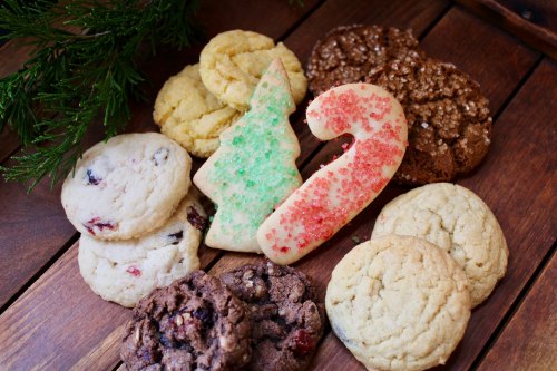 A variety of festive cookies, including a green tree and red candy cane, arranged on a wooden surface.