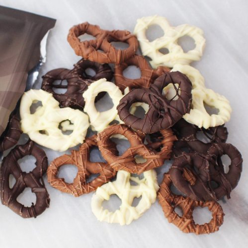 A pile of chocolate-covered pretzels in dark, milk, and white chocolate on a marble surface.