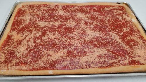 A rectangular pizza dough topped with a layer of tomato sauce and sprinkled with cheese, ready for baking.