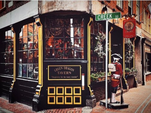 Historic tavern with a sign reading "Green Dragon Tavern," featuring festive decorations and a soldier statue outside.