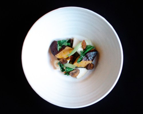 A white bowl filled with colorful vegetables, including greens and chunks of yellow squash, on a dark background.