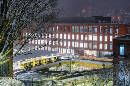 A snowy scene featuring a modern building with illuminated windows and a light rail station below.
