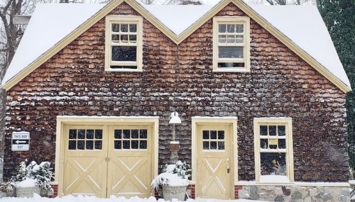 A charming wooden house with a shingled exterior, covered in snow, featuring yellow doors and windows.