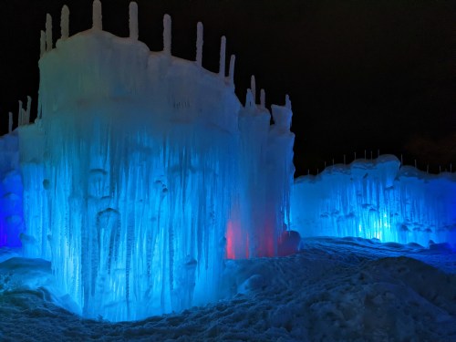 Colorful ice formations illuminated in blue and red light, creating a magical winter landscape at night.