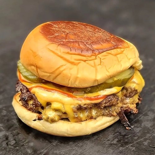 A juicy cheeseburger with melted cheese, pickles, and ketchup on a toasted bun, resting on a dark surface.