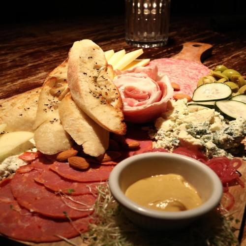 A beautifully arranged charcuterie board with meats, cheeses, fruits, nuts, and a small bowl of mustard.