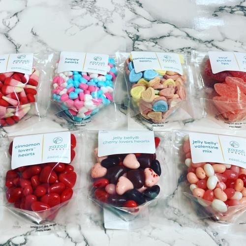 Assorted colorful candies in clear bags, including hearts and jelly beans, arranged on a marble surface.