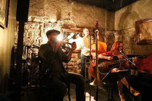 A jazz trio performs in a dimly lit venue, featuring a trumpet player, a bassist, and a guitarist.