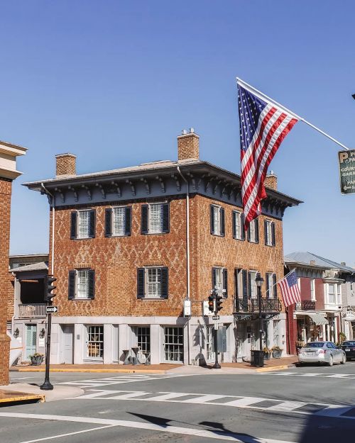 Historic brick building at a street corner, featuring American flags and clear blue skies.