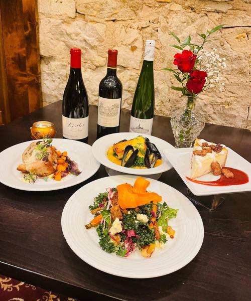 A table set with gourmet dishes, wine bottles, and a vase of roses, featuring salads, seafood, and a dessert.