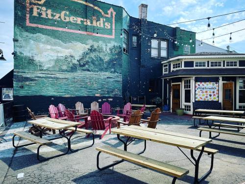 Outdoor seating area with picnic tables and colorful chairs in front of a mural at FitzGerald's. Bright, sunny day.