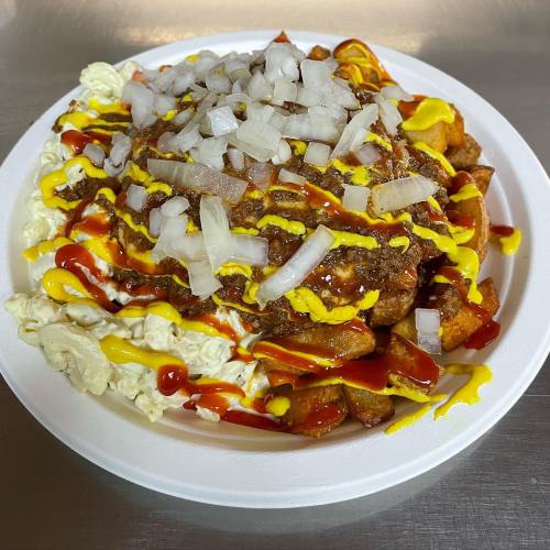A plate of loaded fries topped with chili, onions, mustard, ketchup, and drizzled sauces.