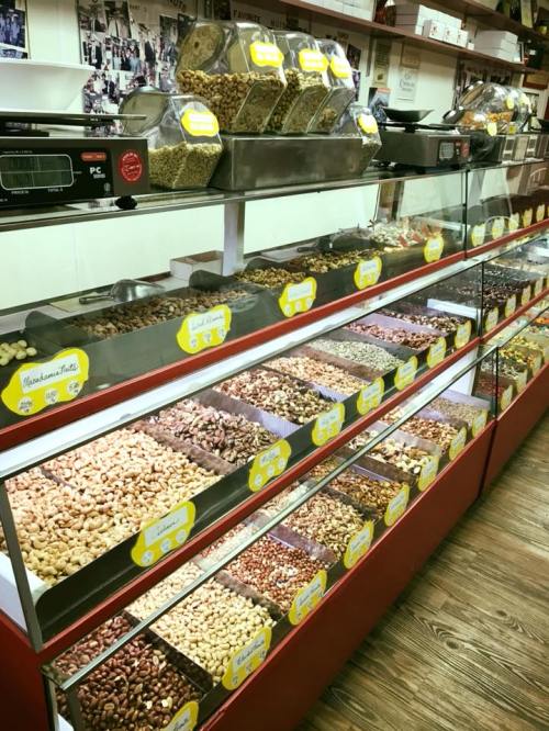 A display case filled with various types of nuts and dried fruits, labeled and organized in a shop setting.