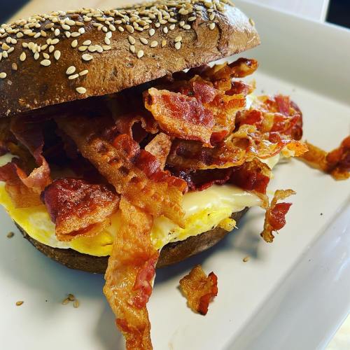 A sesame seed bagel filled with crispy bacon and a fluffy egg, served on a white plate.