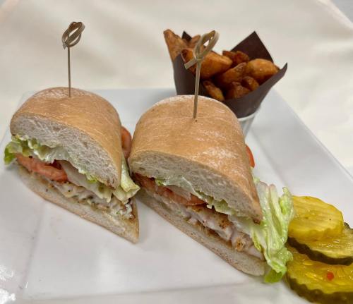 A sandwich with lettuce, tomato, and chicken, served with pickles and a side of crispy potato wedges.