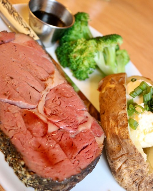A plate featuring sliced roast beef, steamed broccoli, and a baked potato topped with sour cream and green onions.