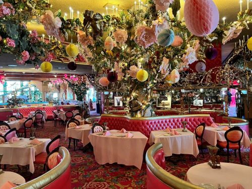 Colorful restaurant interior with floral decorations, chandeliers, and pink seating, creating a whimsical atmosphere.