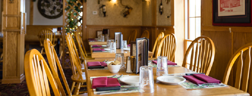 A cozy restaurant interior with wooden tables, chairs, and neatly set dining utensils.