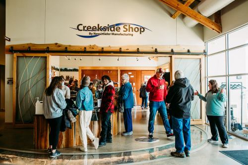 A busy shop interior with people browsing and chatting, featuring a wooden counter and large windows.