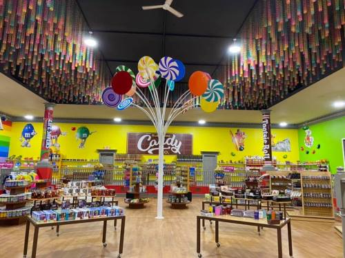 Colorful candy store interior with vibrant decorations, shelves filled with sweets, and a whimsical lollipop tree centerpiece.