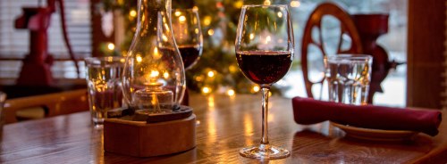 A cozy table setting with a glass of red wine, a lantern, and soft lighting from nearby candles.