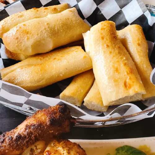 A basket of golden, crispy breadsticks served on a checkered paper liner.